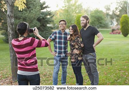 Stock Image - Woman taking picture of friends in park. Fotosearch