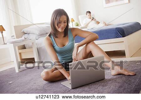 Woman using laptop with husband on lounger in background View Large Photo Image Stock Image - Woman using laptop with husband on lounger in background. Fotosearch