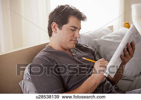 Young man laying on bed filling crossword View Large Photo Image Stock Photo - Young man laying on bed filling crossword. Fotosearch