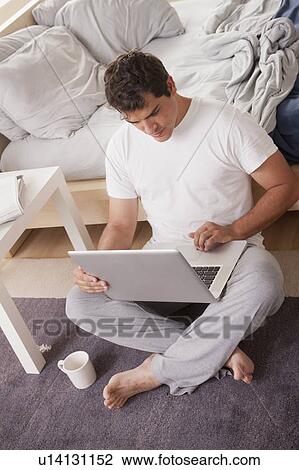 Stock Image - Young men in pajamas using laptop. Fotosearch
