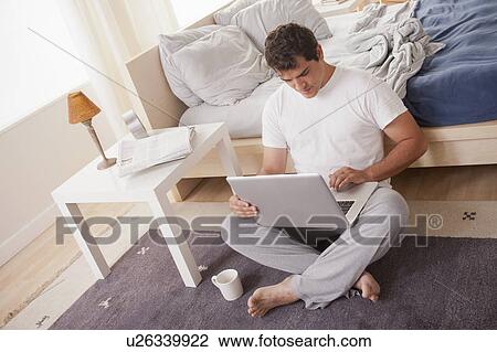 Stock Image - Young men in pajamas using laptop. Fotosearch