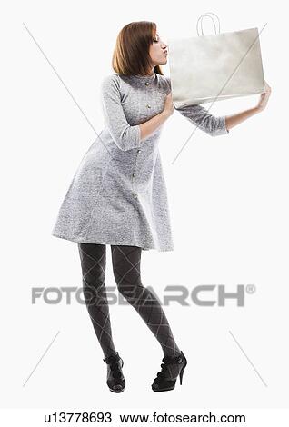 Stock Image - Young woman holding shopping bag, studio shot. Fotosearch