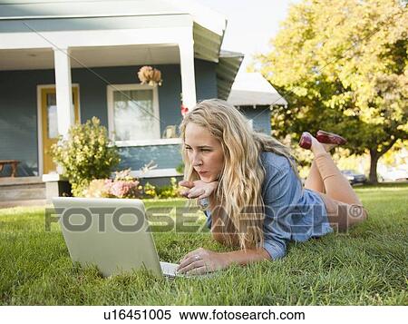 Young woman lying down on grass with her laptop, blowing a kiss View Large Photo Image Stock Photography - Young woman lying down on grass with her laptop, blowing a kiss. Fotosearch