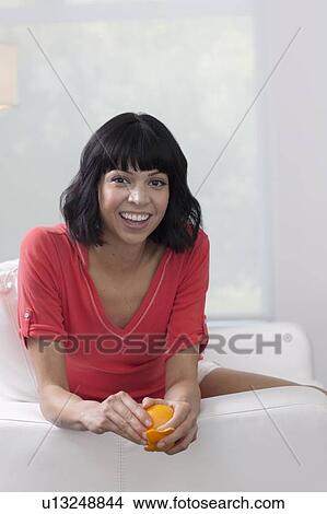 Young woman sitting on sofa and eating orange View Large Photo Image Picture - Young woman sitting on sofa and eating orange. Fotosearch