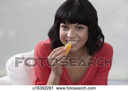 Young woman sitting on sofa and eating orange View Large Photo Image Stock Image - Young woman sitting on sofa and eating orange. Fotosearch