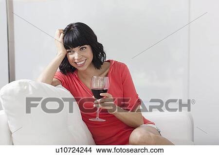 Young woman sitting on sofa with glass of wine View Large Photo Image Picture - Young woman sitting on sofa with glass of wine. Fotosearch