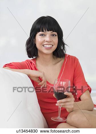 Young woman sitting on sofa with glass of wine View Large Photo Image Stock Image - Young woman sitting on sofa with glass of wine. Fotosearch