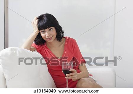 Young woman sitting on sofa with glass of wine View Large Photo Image Stock Photo - Young woman sitting on sofa with glass of wine. Fotosearch