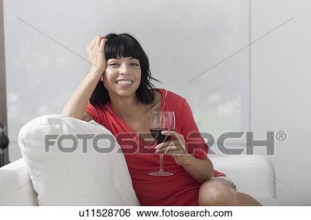 Young woman sitting on sofa with glass of wine View Large Photo Image Stock Photograph - Young woman sitting on sofa with glass of wine. Fotosearch