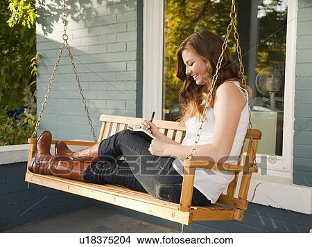 Picture - Young woman sitting on swing and making notes. Fotosearch