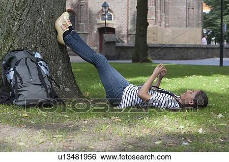 Stock Photograph - Young woman with backpack lying on grass. Fotosearch