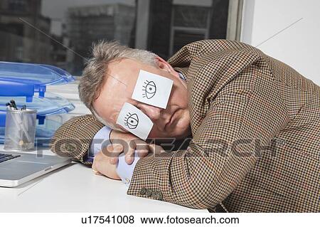 Businessman sleeping with sticky notes on eyes at desk in office View Large Photo Image Stock Photo - Businessman sleeping with sticky notes on eyes at desk in office. Fotosearch