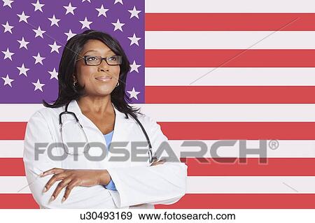 Confident mixed race female surgeon looking away over American flag View Large Photo Image Stock Photo - Confident mixed race female surgeon looking away over American flag. Fotosearch