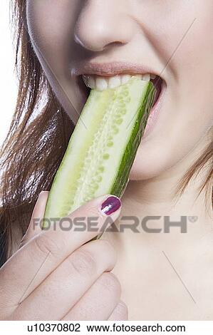 Stock Image - Detail shot of woman eating cucumber over white background. Fotosearch