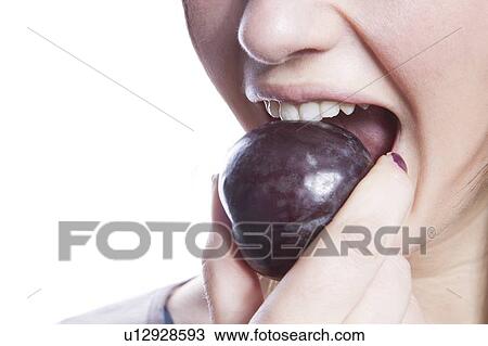 Stock Image - Detail shot of young woman eating plum over white background. Fotosearch