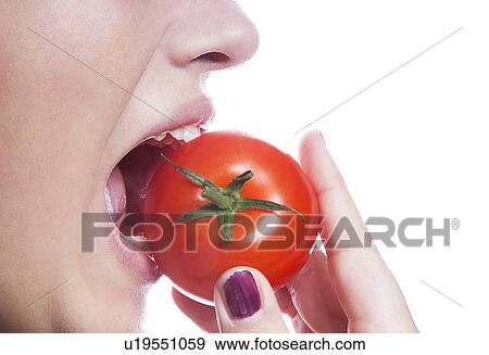 Stock Photo - Detail shot of young woman eating tomato over white background. Fotosearch