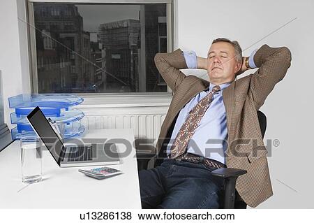 Middle-aged businessman resting on chair in front of laptop in office View Large Photo Image Stock Photo - Middle-aged businessman resting on chair in front of laptop in office. Fotosearch