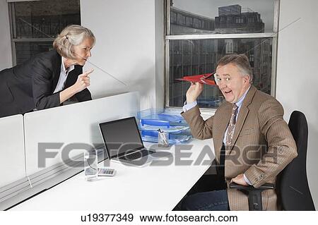 Middle-aged businessman throwing paper airplane towards female colleague in office View Large Photo Image Stock Photo - Middle-aged businessman throwing paper airplane towards female colleague in office. Fotosearch