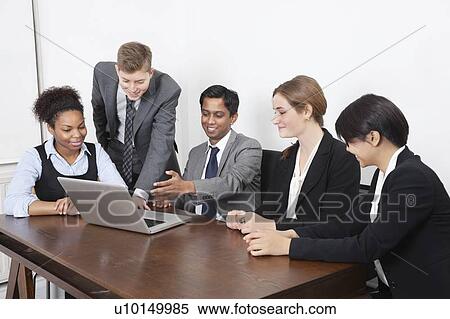 Stock Photography - Multiethnic professionals using laptop at conference room. Fotosearch