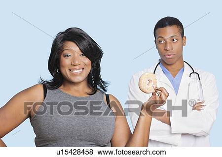 Overweight mixed race woman with donut by doctor over blue background View Large Photo Image Stock Photo - Overweight mixed race woman with donut by doctor over blue background. Fotosearch