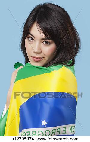 Picture - Patriotic young woman wrapped in Brazilian flag over blue background. Fotosearch