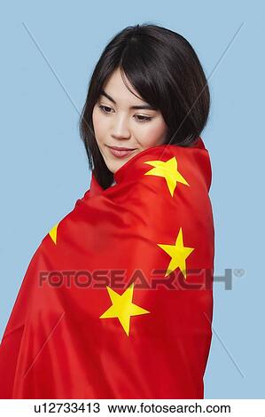 Stock Image - Patriotic young woman wrapped in Chinese flag over blue background. Fotosearch