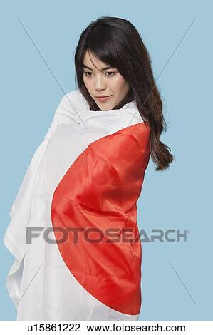 Stock Image - Patriotic young woman wrapped in Japanese flag over blue background. Fotosearch