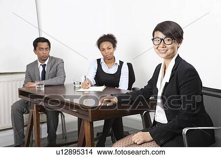 Picture - Portrait of Asian female with multiethnic colleagues in background at desk in office. Fotosearch
