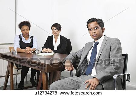 Portrait of Asian male with female colleagues in background at desk in office View Large Photo Image Stock Photo - Portrait of Asian male with female colleagues in background at desk in office. Fotosearch