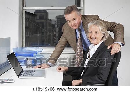 Stock Photograph - Portrait of businesswoman and man with laptop at desk in office. Fotosearch