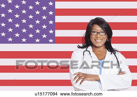 Picture - Portrait of confident mixed race female surgeon over American flag. Fotosearch