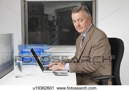 Portrait of middle-aged businessman using laptop at desk in office View Large Photo Image Stock Image - Portrait of middle-aged businessman using laptop at desk in office. Fotosearch