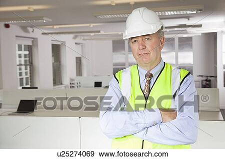 Stock Photo - Portrait of middle-aged man in reflector vest and hard hat at office. Fotosearch