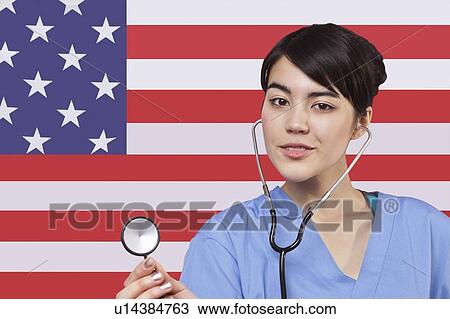 Stock Image - Portrait of mixed race female surgeon standing over American flag. Fotosearch
