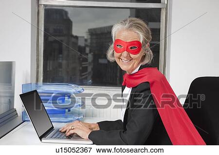 Portrait of senior businesswoman in superhero costume using laptop at office desk View Large Photo Image Stock Photo - Portrait of senior businesswoman in superhero costume using laptop at office desk. Fotosearch