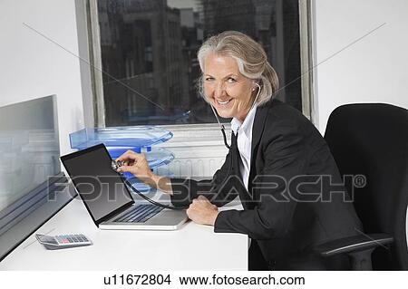 Portrait of senior businesswoman examining laptop with the use of stethoscope at office desk View Large Photo Image Picture - Portrait of senior businesswoman examining laptop with the use of stethoscope at office desk. Fotosearch