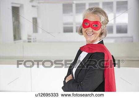 Stock Image - Portrait of smiling senior businesswoman in superhero costume in office. Fotosearch