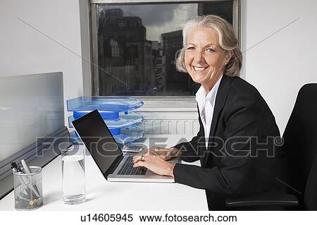 Portrait of smiling senior businesswoman using laptop at desk in office View Large Photo Image Stock Photography - Portrait of smiling senior businesswoman using laptop at desk in office. Fotosearch