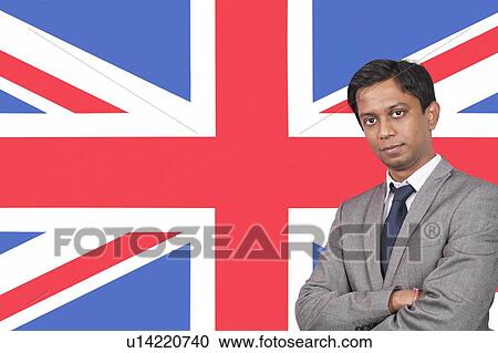 Stock Image - Portrait of young businessman with arms crossed over British flag. Fotosearch