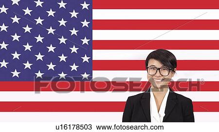 Stock Image - Portrait of young businesswoman smiling over American flag. Fotosearch
