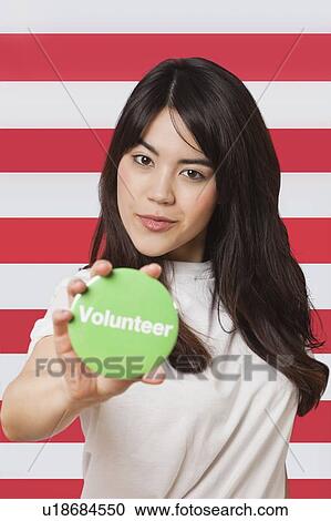 Portrait of young woman holding out volunteer badge against American flag View Large Photo Image Stock Image - Portrait of young woman holding out volunteer badge against American flag. Fotosearch