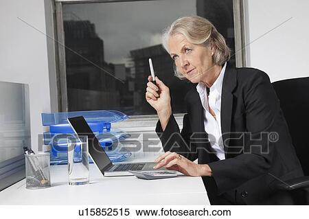 Senior businesswoman using laptop and calculator at desk in office View Large Photo Image Stock Photography - Senior businesswoman using laptop and calculator at desk in office. Fotosearch