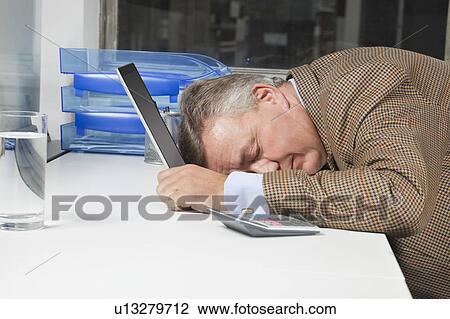 Stock Image - Side view of exhausted businessman with head on laptop in office. Fotosearch