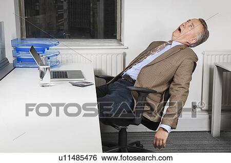 Stock Photograph - Side view of exhausted middle-aged businessman in front of laptop in office. Fotosearch