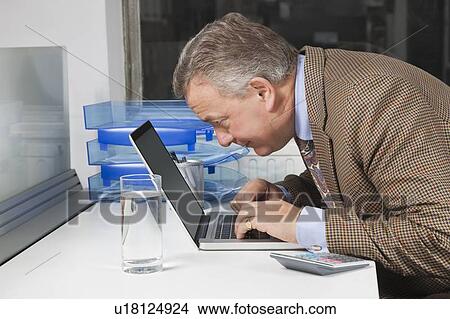 Picture - Side view of middle-aged businessman using laptop at desk in office. Fotosearch