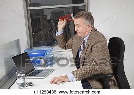 Side view of middle-aged businessman throwing paper airplane in office View Large Photo Image Stock Photograph - Side view of middle-aged businessman throwing paper airplane in office. Fotosearch