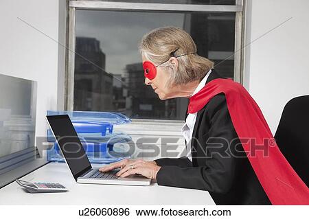 Side view of senior businesswoman in superhero costume using laptop at office desk View Large Photo Image Stock Photograph - Side view of senior businesswoman in superhero costume using laptop at office desk. Fotosearch