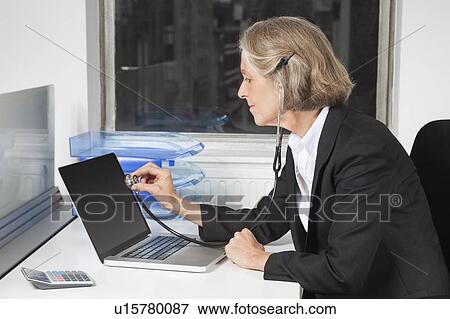 Side view of senior businesswoman examining laptop with the use of stethoscope at office desk View Large Photo Image Stock Photo - Side view of senior businesswoman examining laptop with the use of stethoscope at office desk. Fotosearch