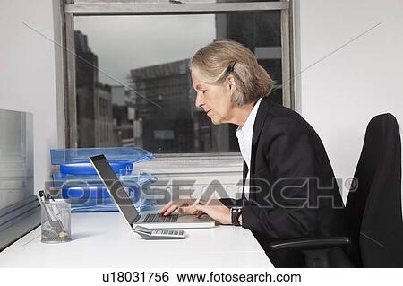 Side view of senior businesswoman using laptop at desk in office View Large Photo Image Stock Photograph - Side view of senior businesswoman using laptop at desk in office. Fotosearch