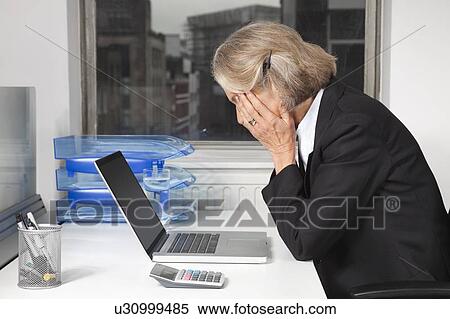 Side view of tired senior businesswoman in front of laptop at desk in office View Large Photo Image Stock Photography - Side view of tired senior businesswoman in front of laptop at desk in office. Fotosearch
